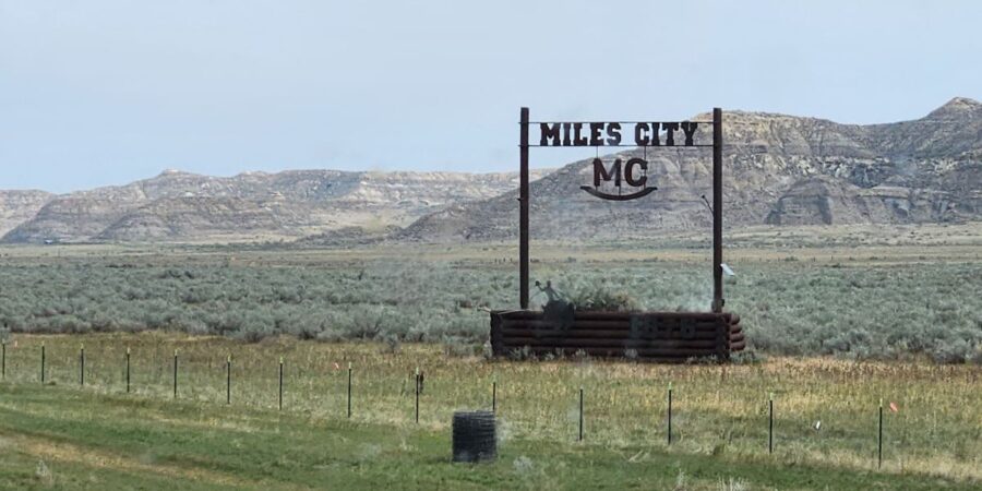 Miles City MC sign on a grassy plain with rocky hills in the background